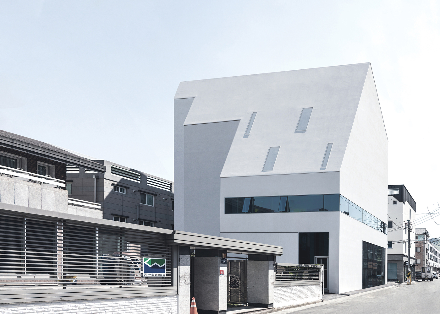 White gabled volume with punched windows and horizontal glass band rising above a street-level commercial facade