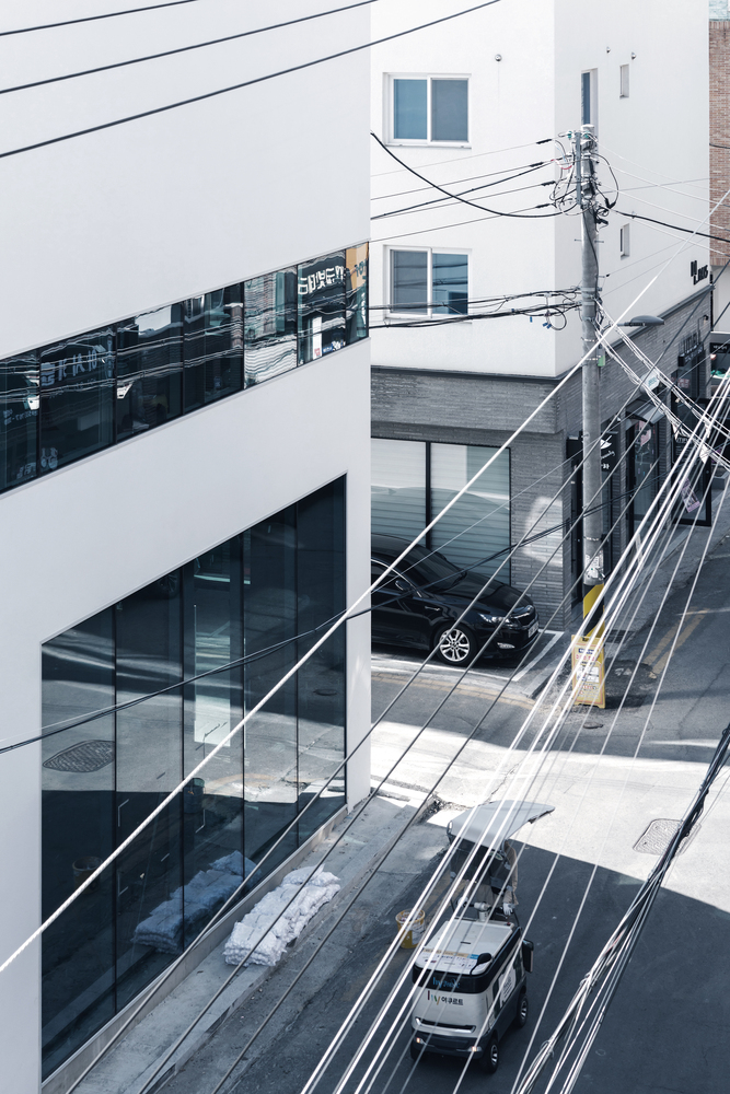 Oblique view showing the horizontal ribbon window wrapping the white facade above the wet street