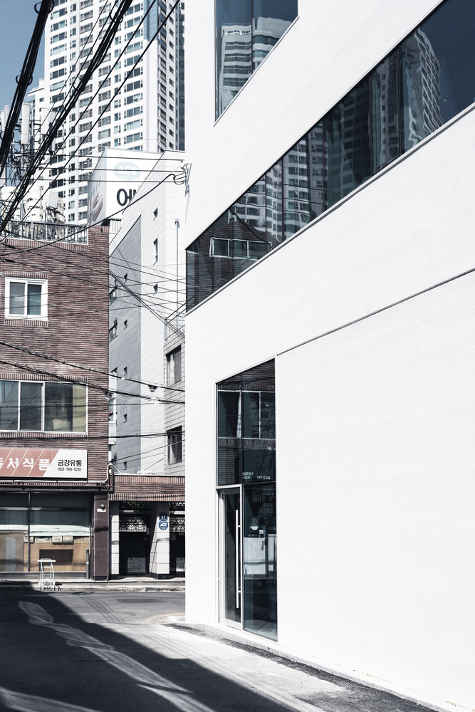 White facade with recessed black-framed glazing slot against neighboring brick buildings and high-rises