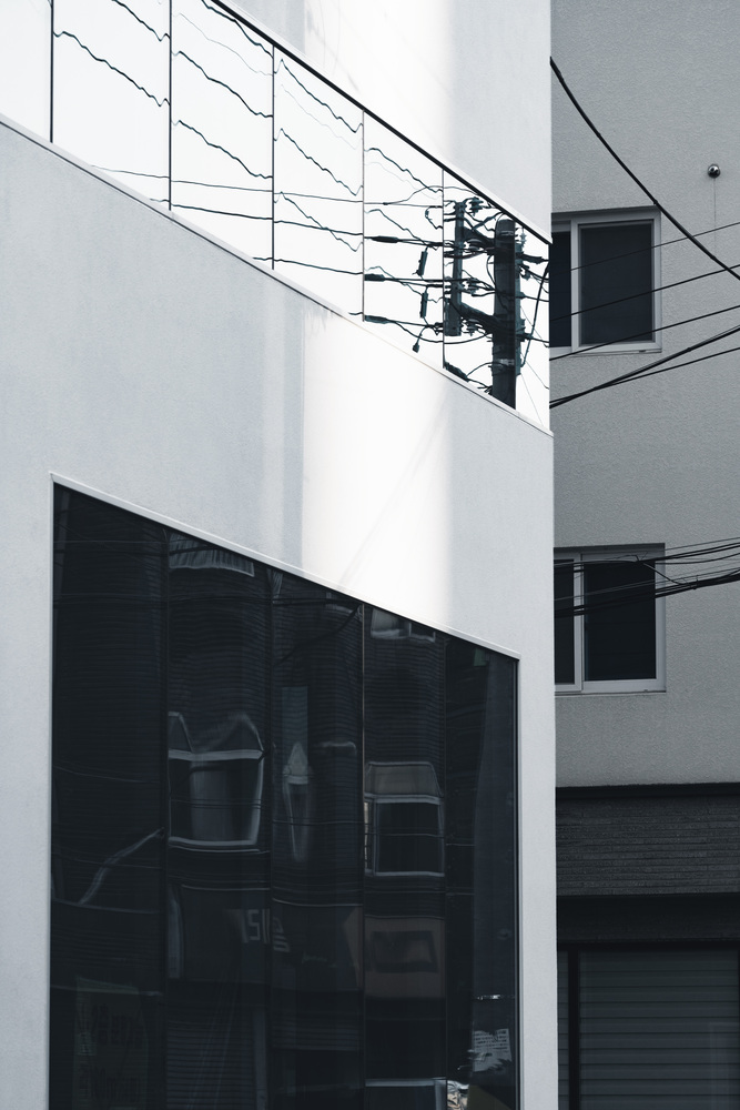 Close-up of the white facade planes with dark glass openings and utility wires crossing overhead