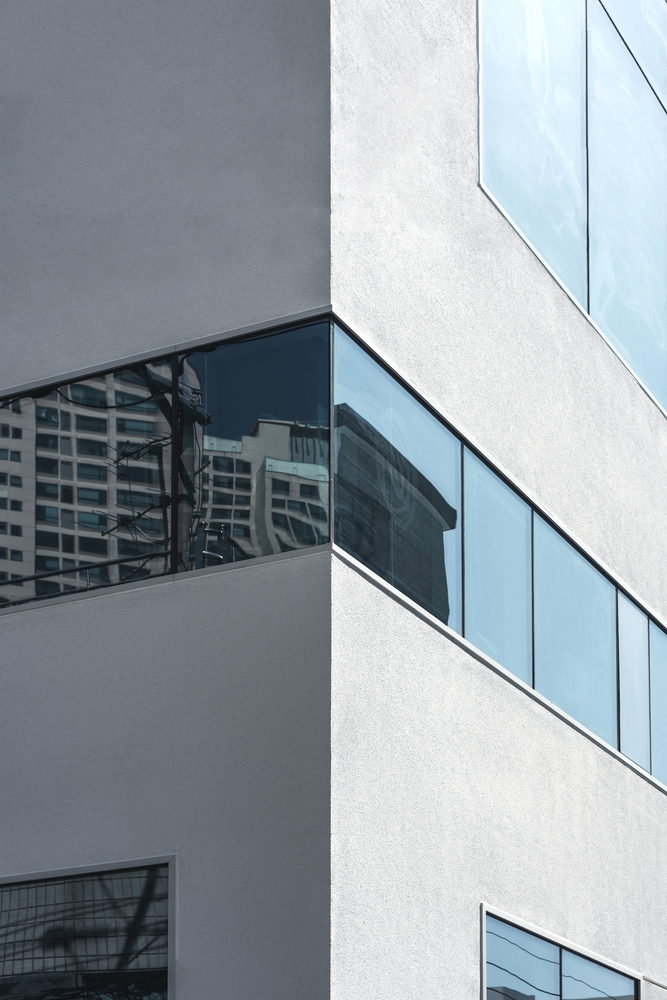 Close-up of white stucco facade with horizontal strip windows reflecting neighboring towers