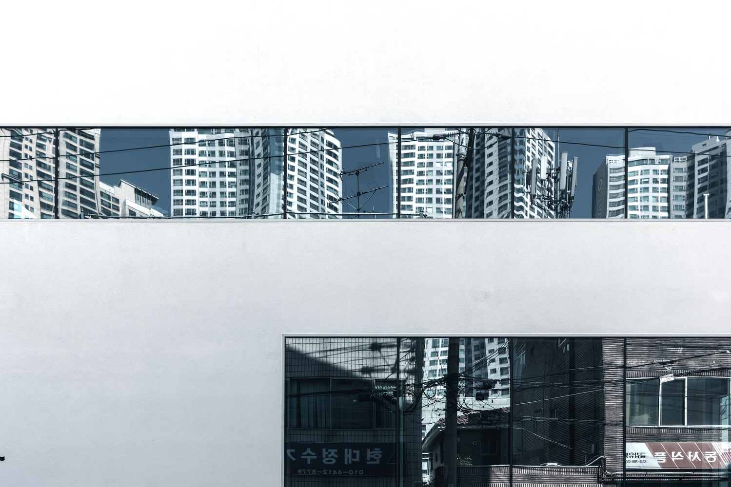 White facade with continuous horizontal ribbon window showing reflections of surrounding high-rise towers