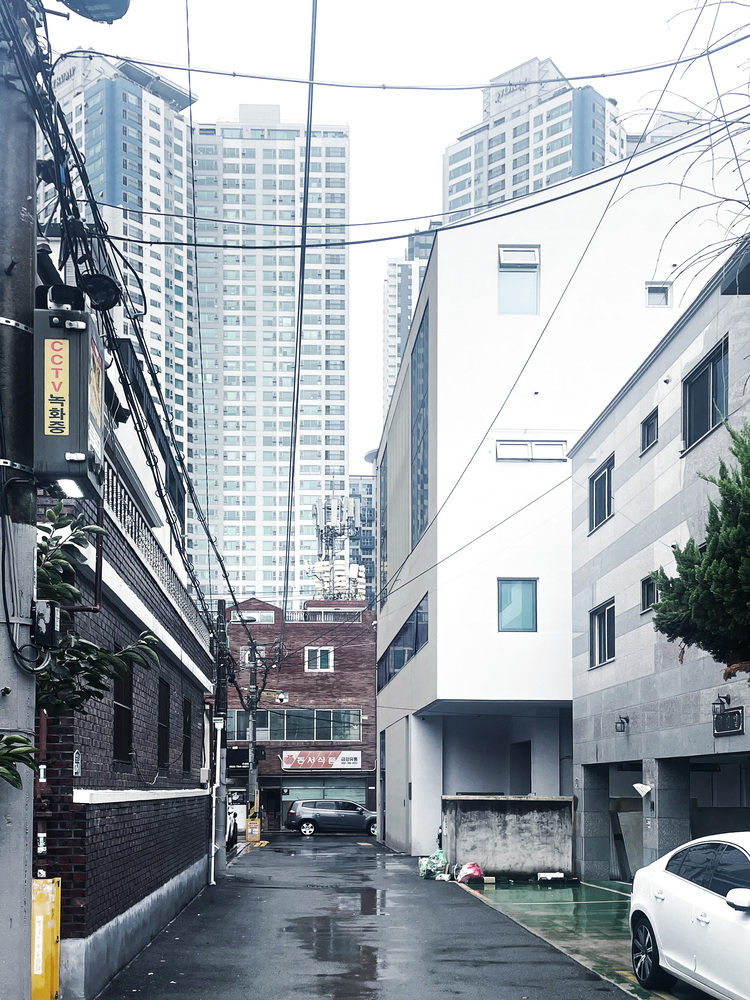 Narrow alley view with white angular volume rising between existing buildings and overhead power lines