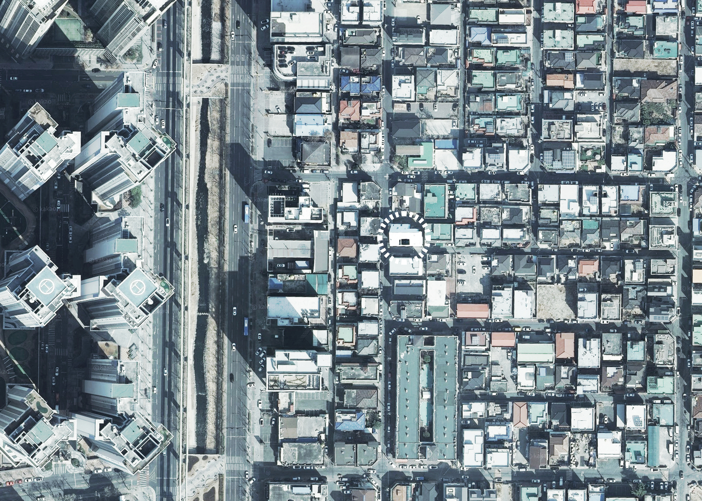 Aerial view showing white angled rooftop inserted within dense gridded neighborhood adjacent to rail corridor