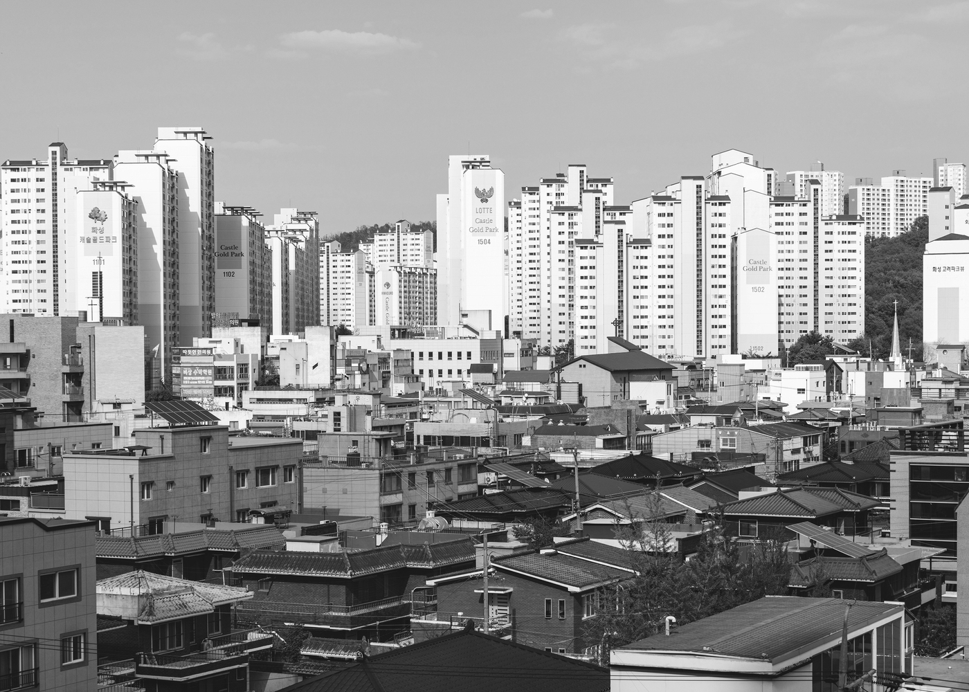Rooftop panorama of low-rise houses and traditional roofs against high-rise residential towers beyond