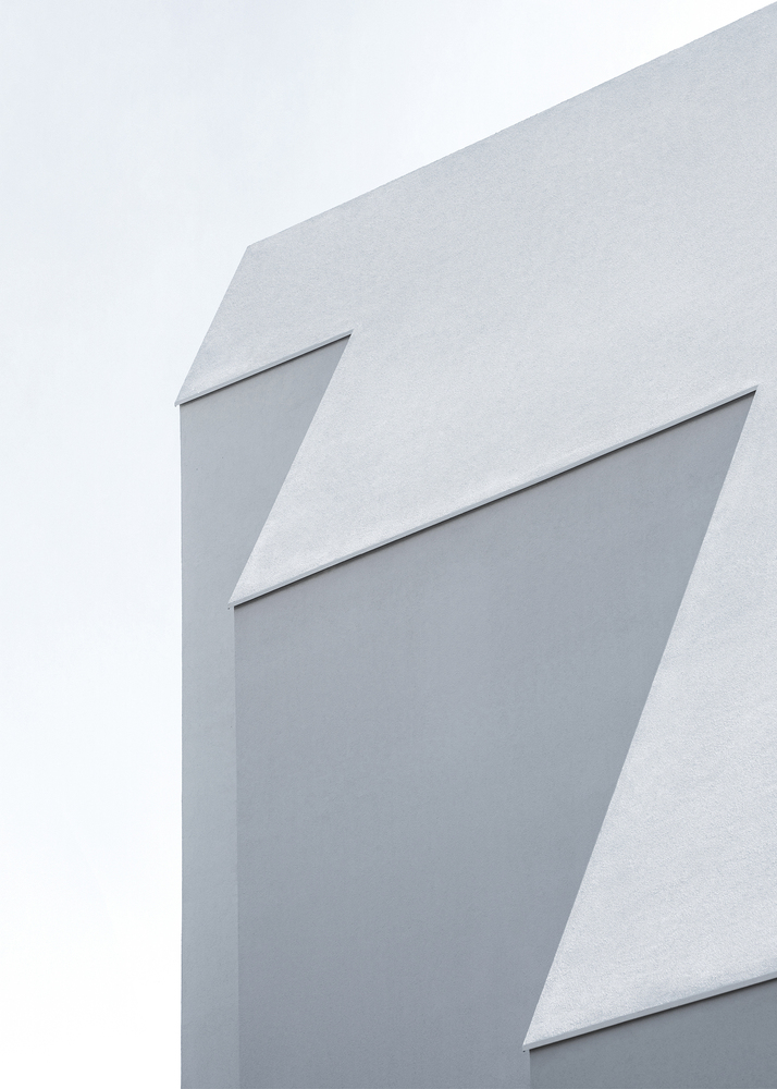 Close-up of white faceted facade with angular recesses against an overcast sky