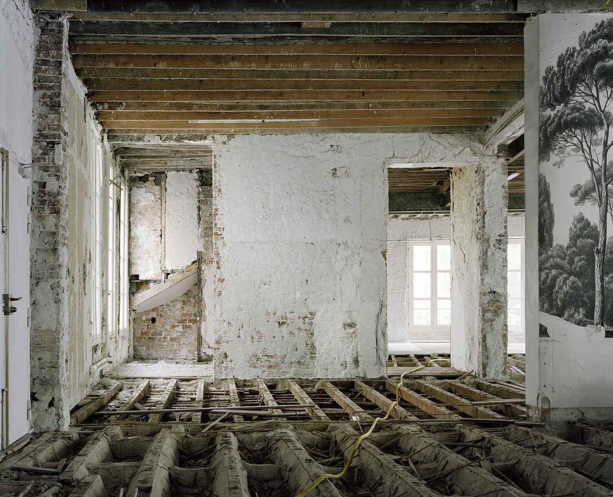 Before: stripped room with exposed timber joists, rubble, brick walls, faded mural wallpaper visible