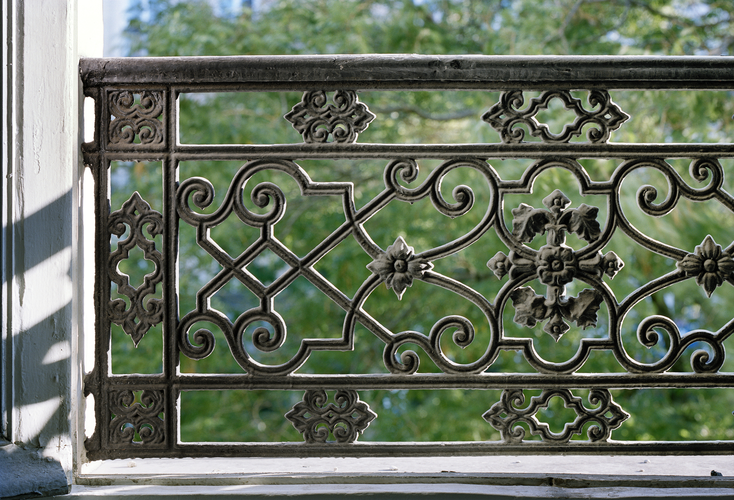 Before: ornate iron balcony railing detail, trees through the bars