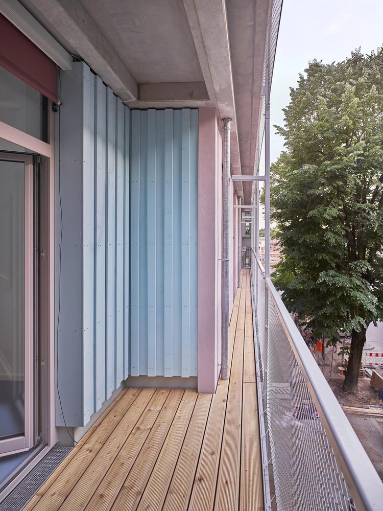 Timber-decked balcony with corrugated metal privacy screen, concrete soffit, and mesh railing overlooking trees