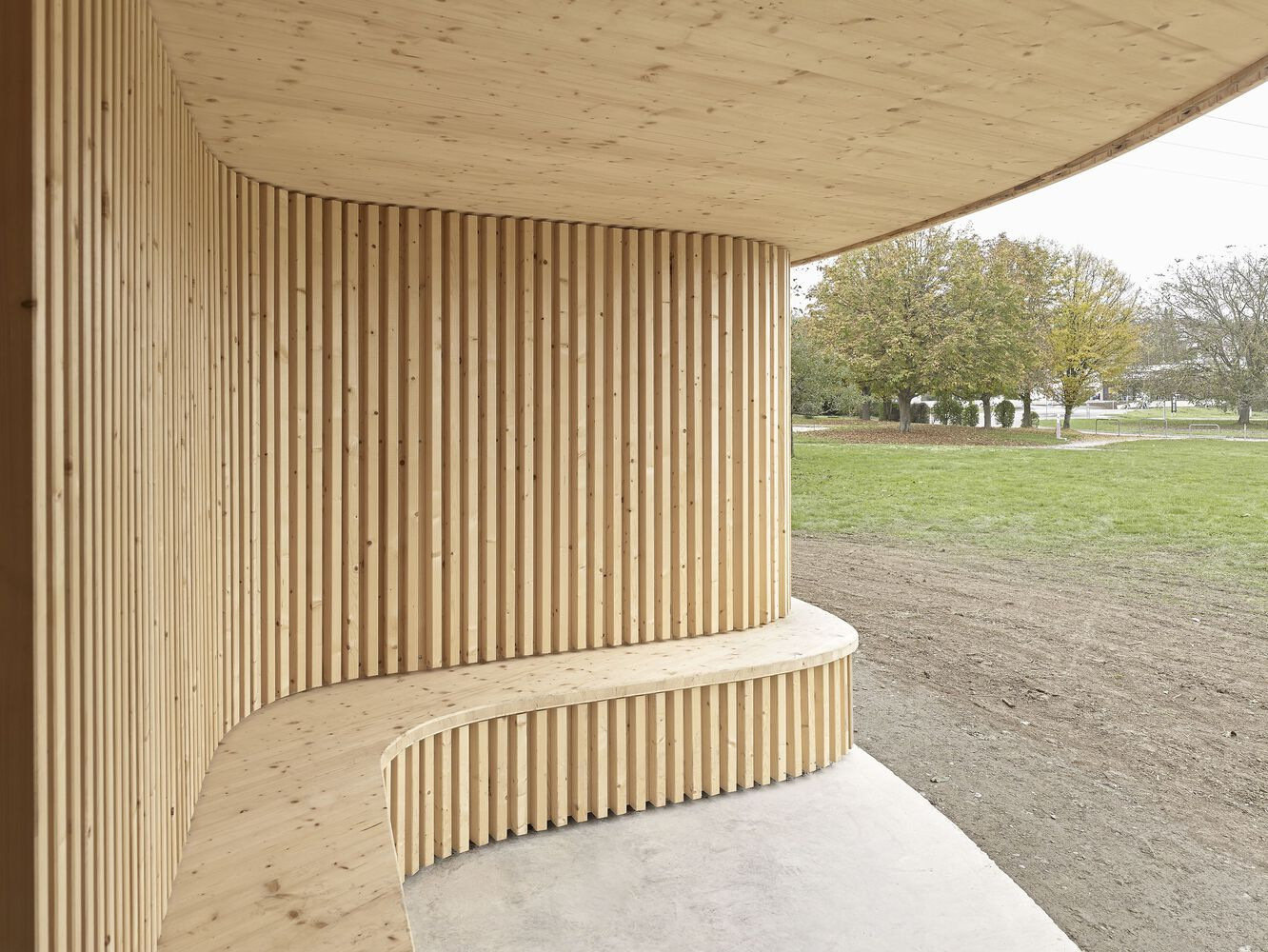 Covered porch with timber slat wall and plywood soffit framing a view toward bare trees