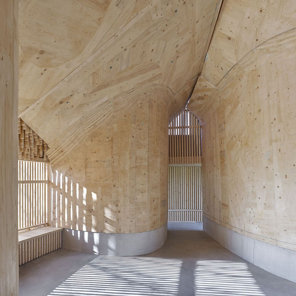 Interior space with arched plywood ceiling and slatted screen casting striped shadows across polished floor