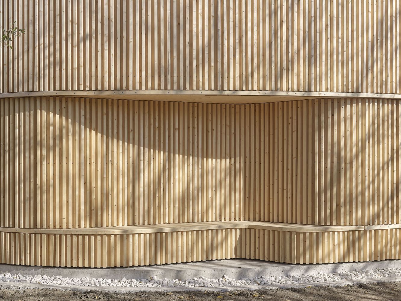 Close-up of the vertical timber slat facade with horizontal banding and white gravel at the base