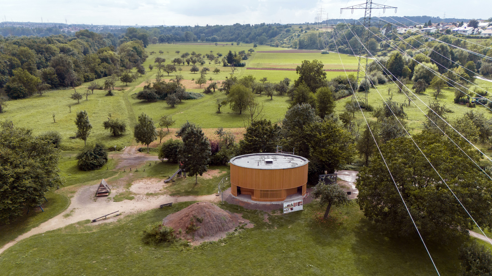 Aerial view of the round timber structure in the park with power lines and scattered trees
