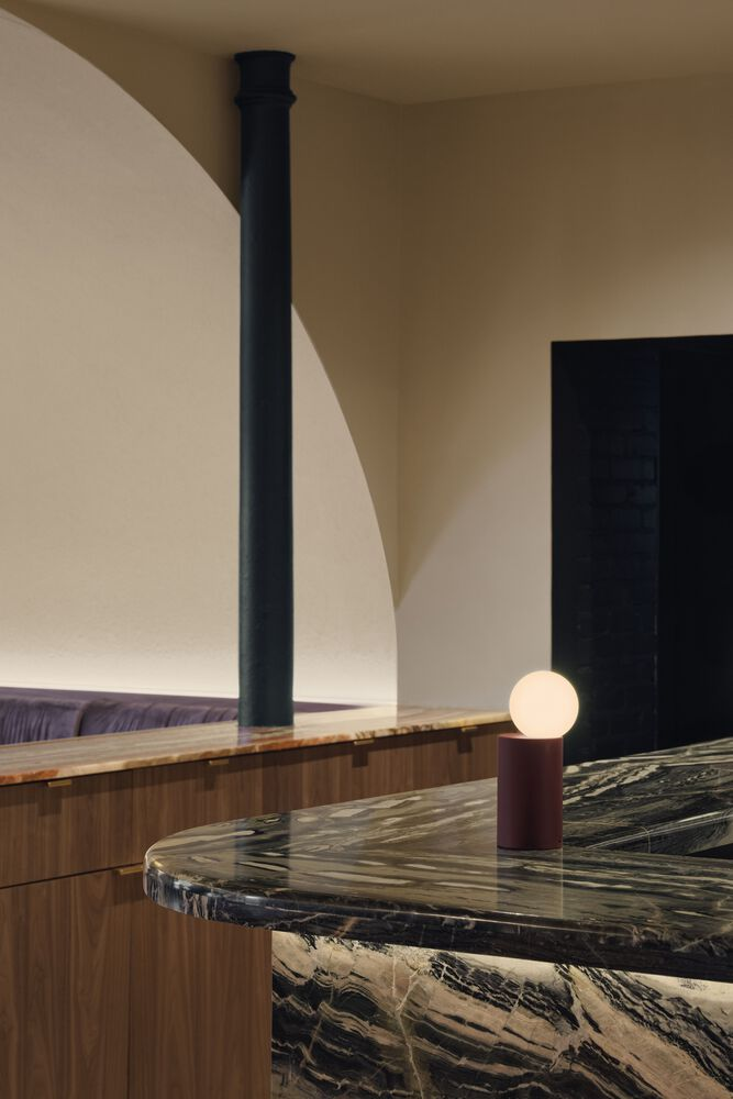 Black marble island counter with veined stone top and spherical table lamp under curved ceiling