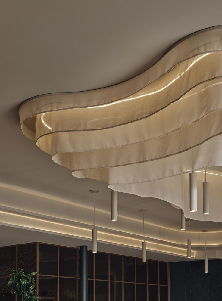 Layered fabric ceiling detail with integrated lighting and suspended cylindrical pendants below