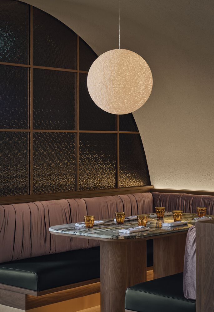Spherical pendant light suspended above a marble-topped table with pink banquette seating and dark textured wall panels