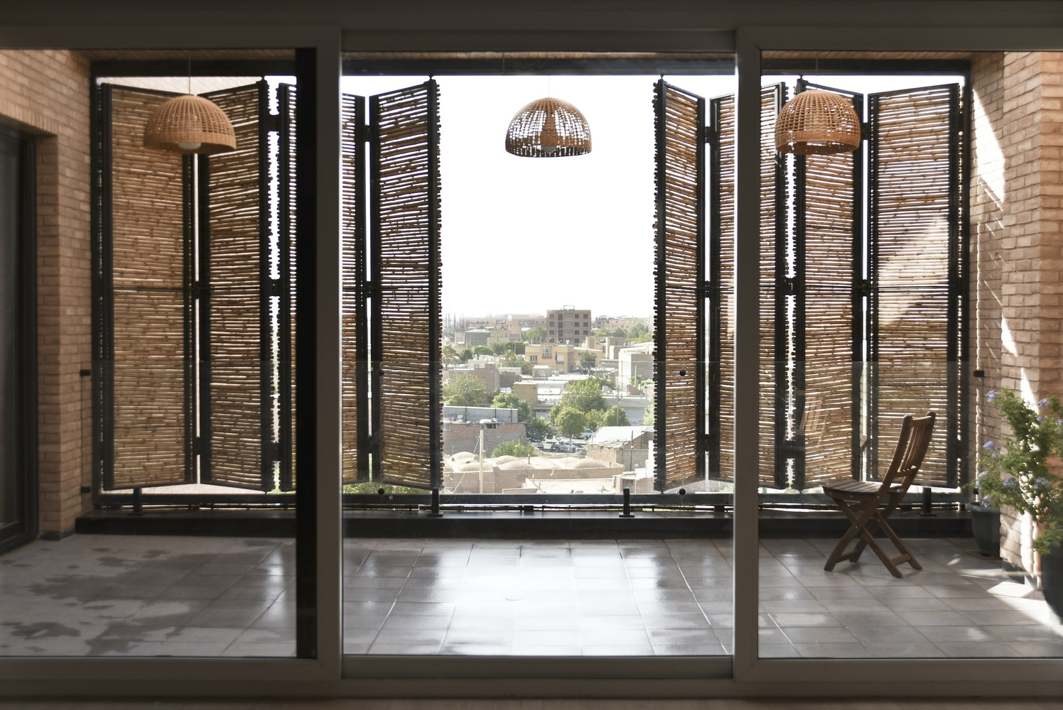 Interior view through sliding glass doors to balcony with folding reed screens and woven pendant lights