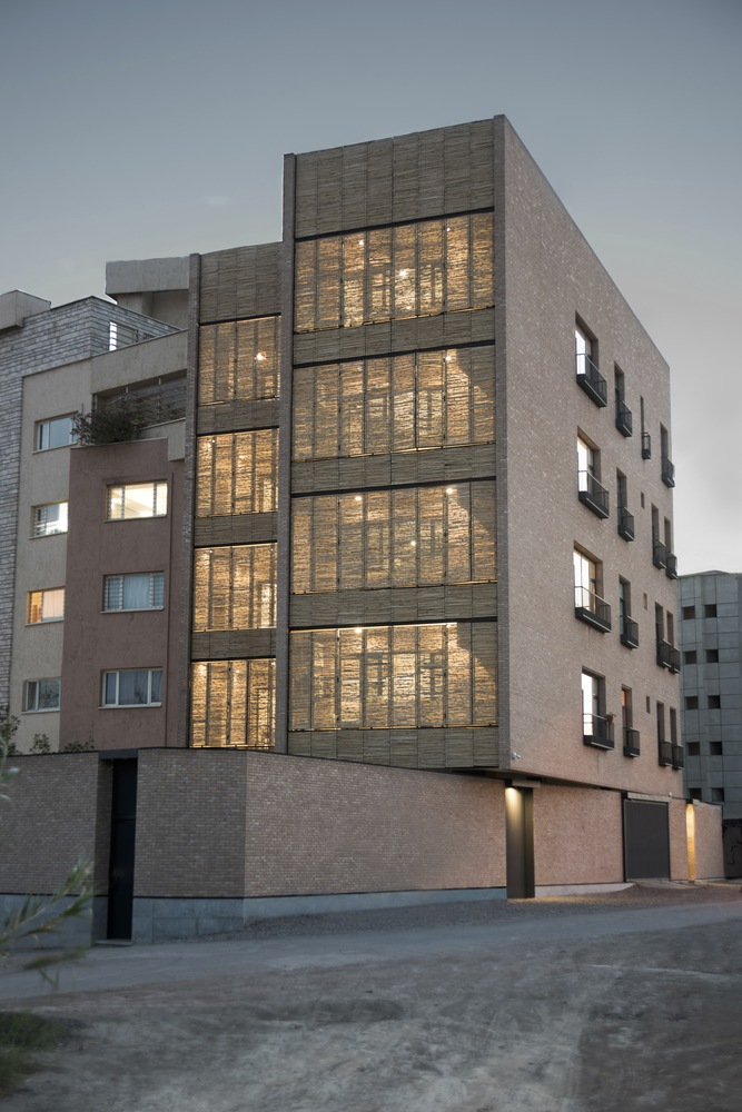 Street facade illuminated at twilight showing vertical bands of woven reed screens behind glass