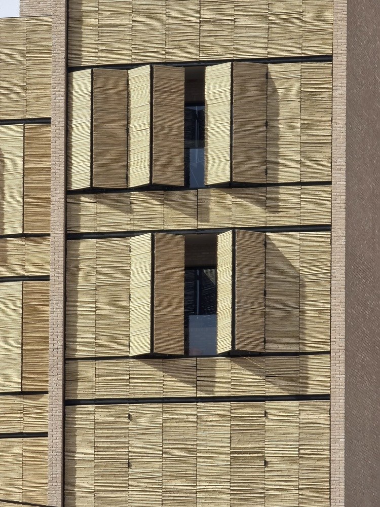 Exterior facade with folding reed shutters framing recessed windows on two levels in direct sunlight