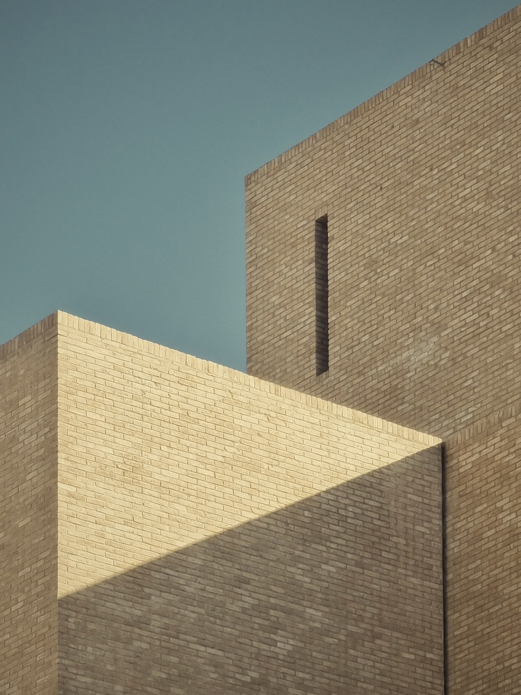 Intersecting brick volumes with a narrow vertical window slot against a clear blue sky