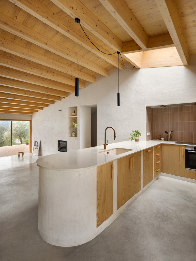 Kitchen pass-through: curved plaster island, brass tap, open shelving with ceramics below, birch timber behind