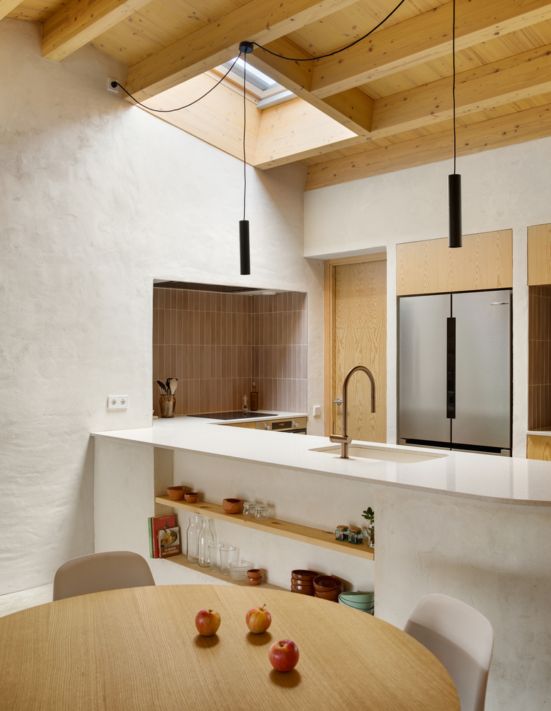 Kitchen tap detail: brass curved tap on white plaster counter, black pendant above, birch plywood behind