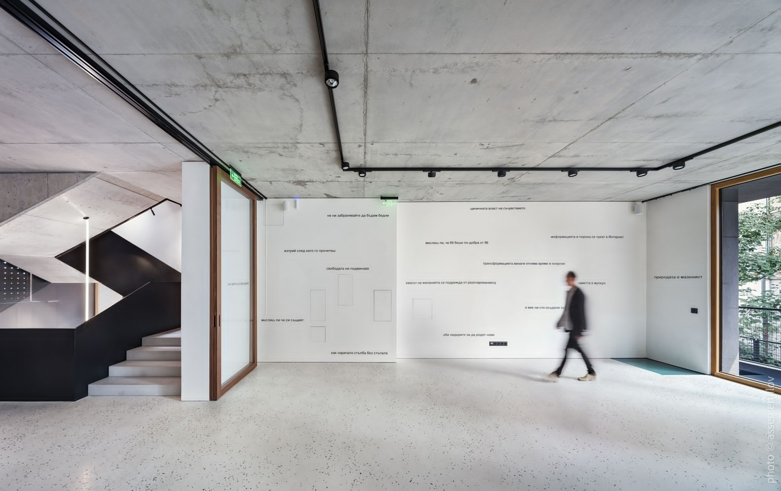 Open gallery space with polished concrete floor, text-filled wall display, and person walking past glazed opening