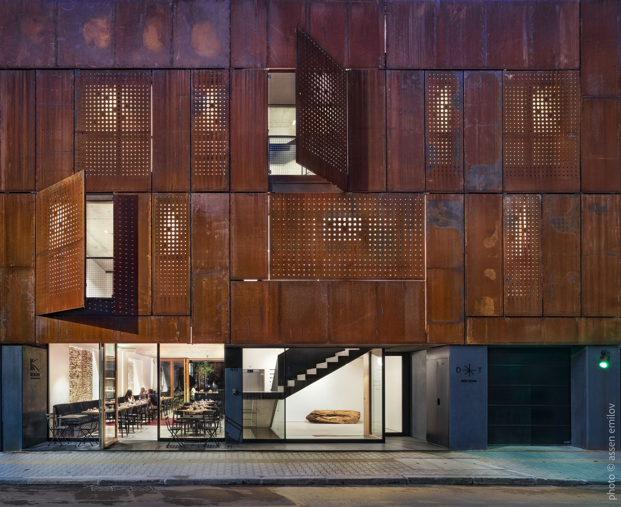 Nighttime view of the perforated corten facade with openings revealing illuminated interior spaces and staircase