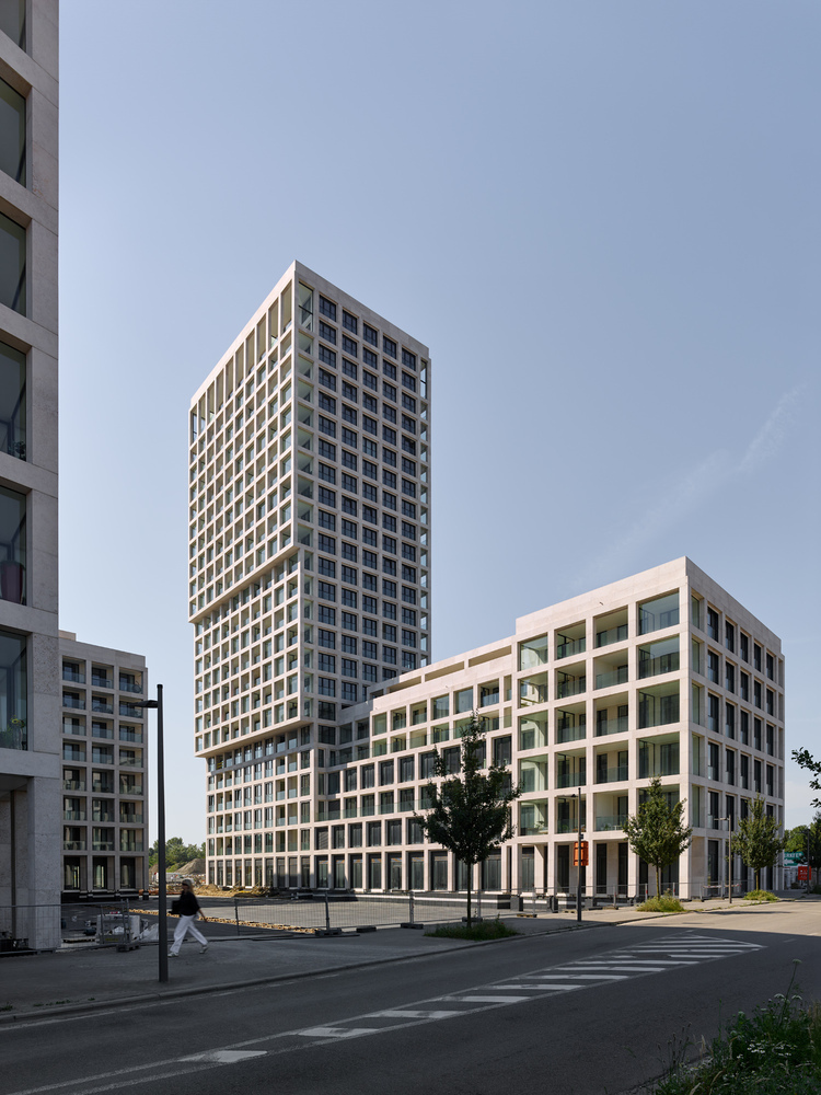 White precast concrete facade grid with deep recessed balconies and a pedestrian crossing the foreground street