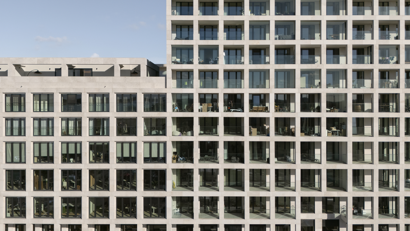 Close-up of the facade grid showing uniform window openings and balcony railings in direct sunlight