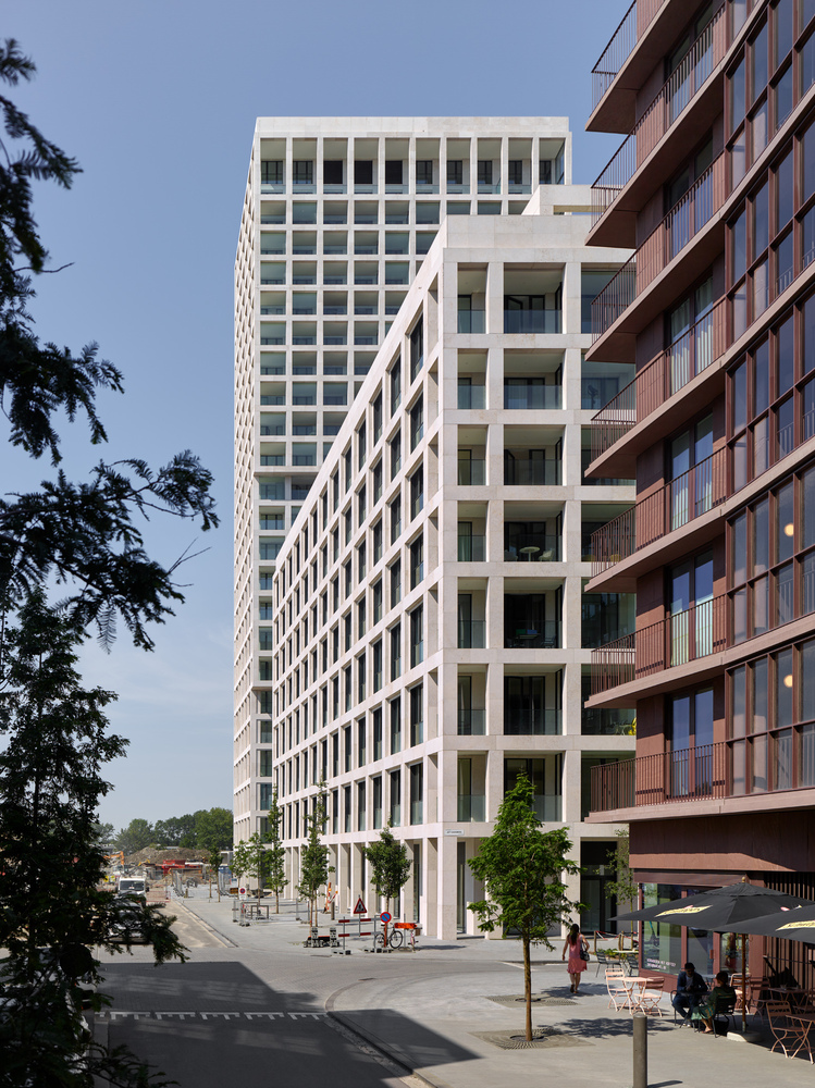 Street-level view of the white tower facade alongside brick residential building with young trees in foreground