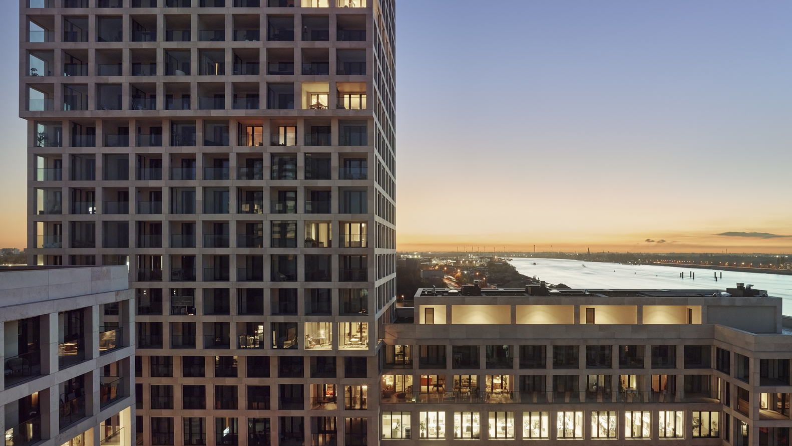 Evening view of illuminated balconies and interior lights glowing across the gridded facade at twilight
