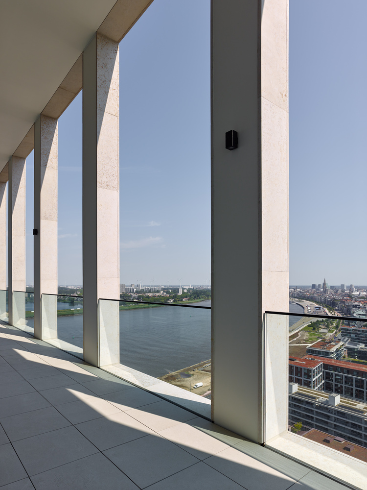 Covered balcony with alternating concrete columns and dark metal mullions framing views of the river and cityscape