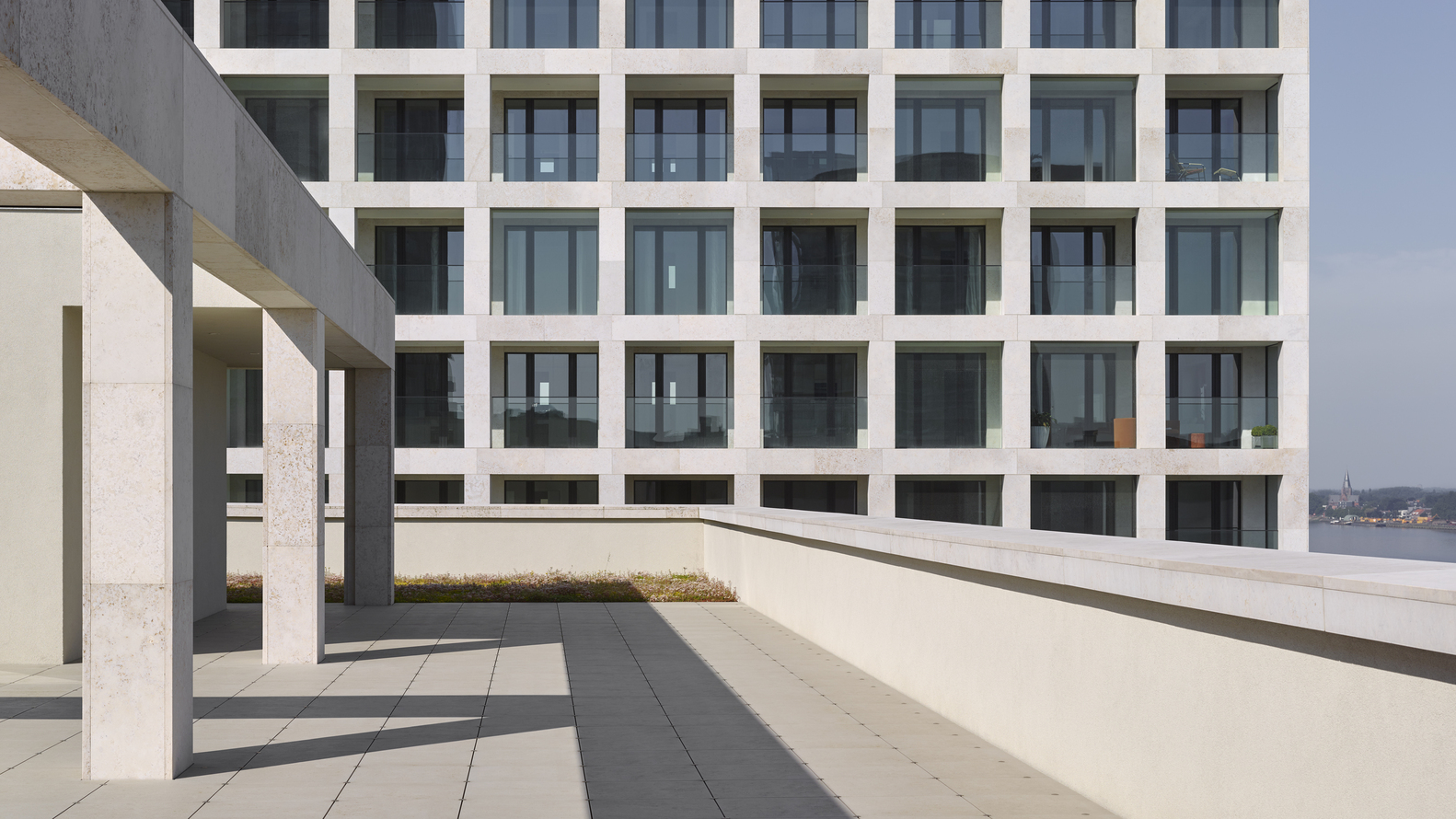 Outdoor terrace with deep shadowed colonnade facing the gridded facade of the adjacent residential tower