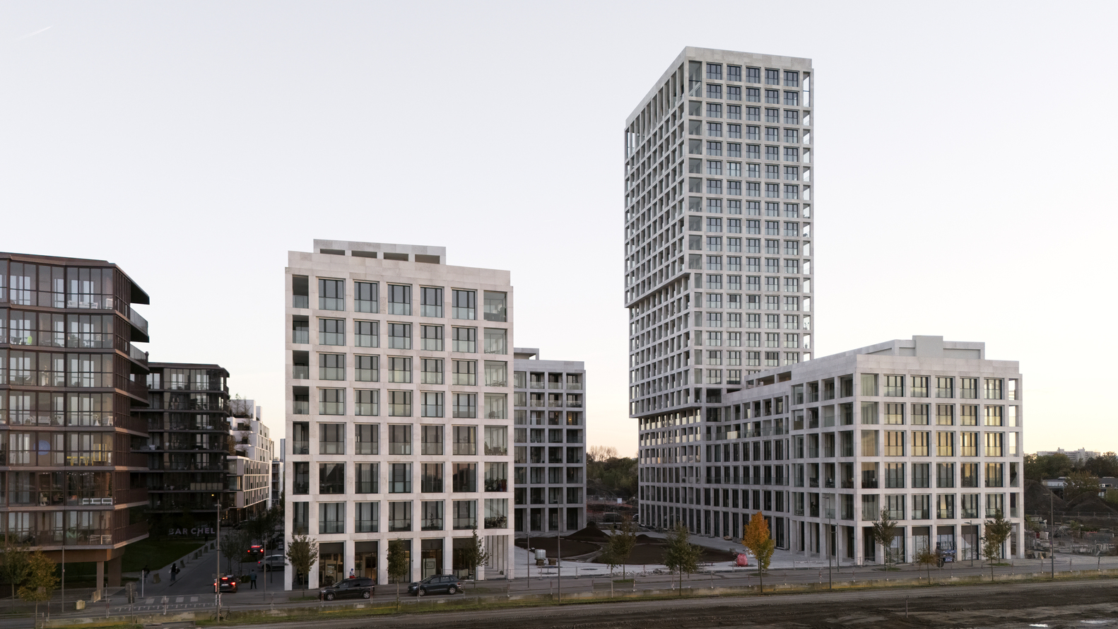 Street view showing three residential towers with gridded facades in the early evening light