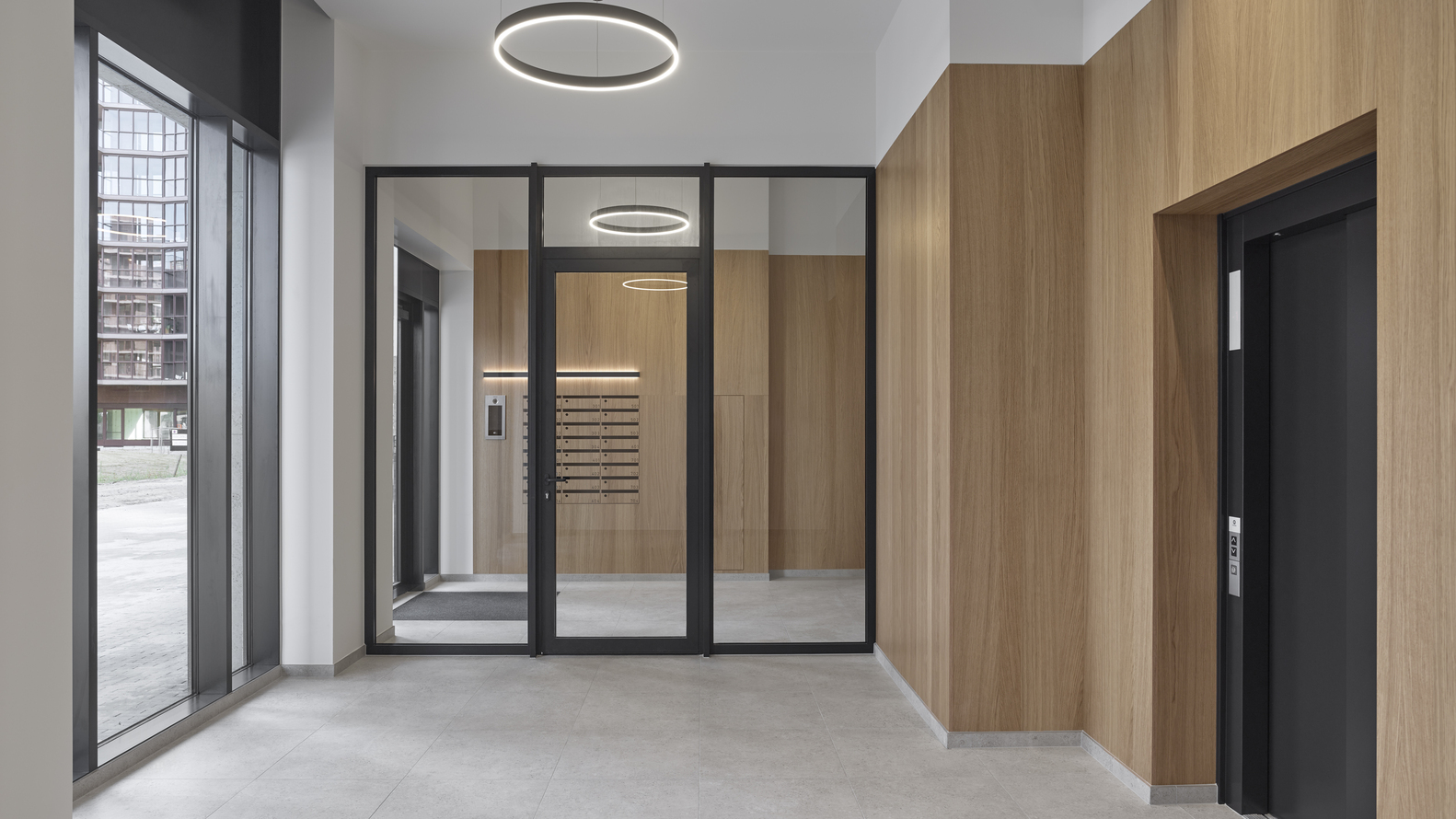 Ground floor lobby with black-framed glass doors, timber veneer walls and circular pendant lights overhead