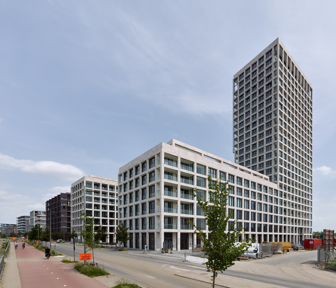 Street view of tiered residential blocks with white concrete frames and glazed balconies under a pale sky