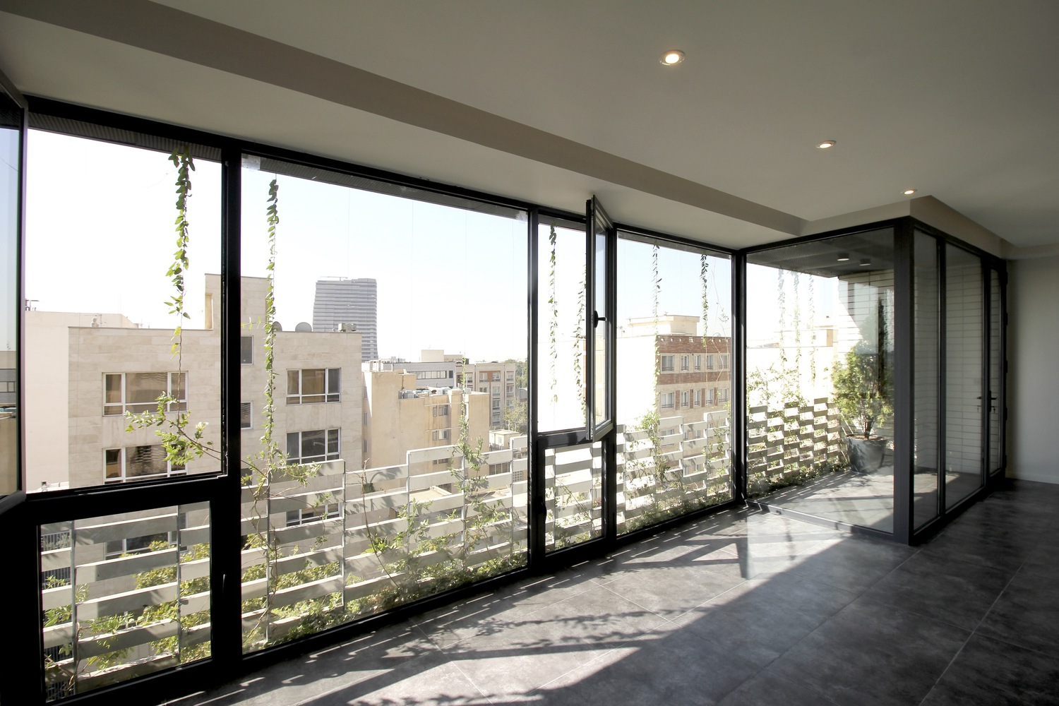 Upper interior: full-height black-framed glazing wrapping a corner, view over neighbouring rooftops, polished dark floor, open living space