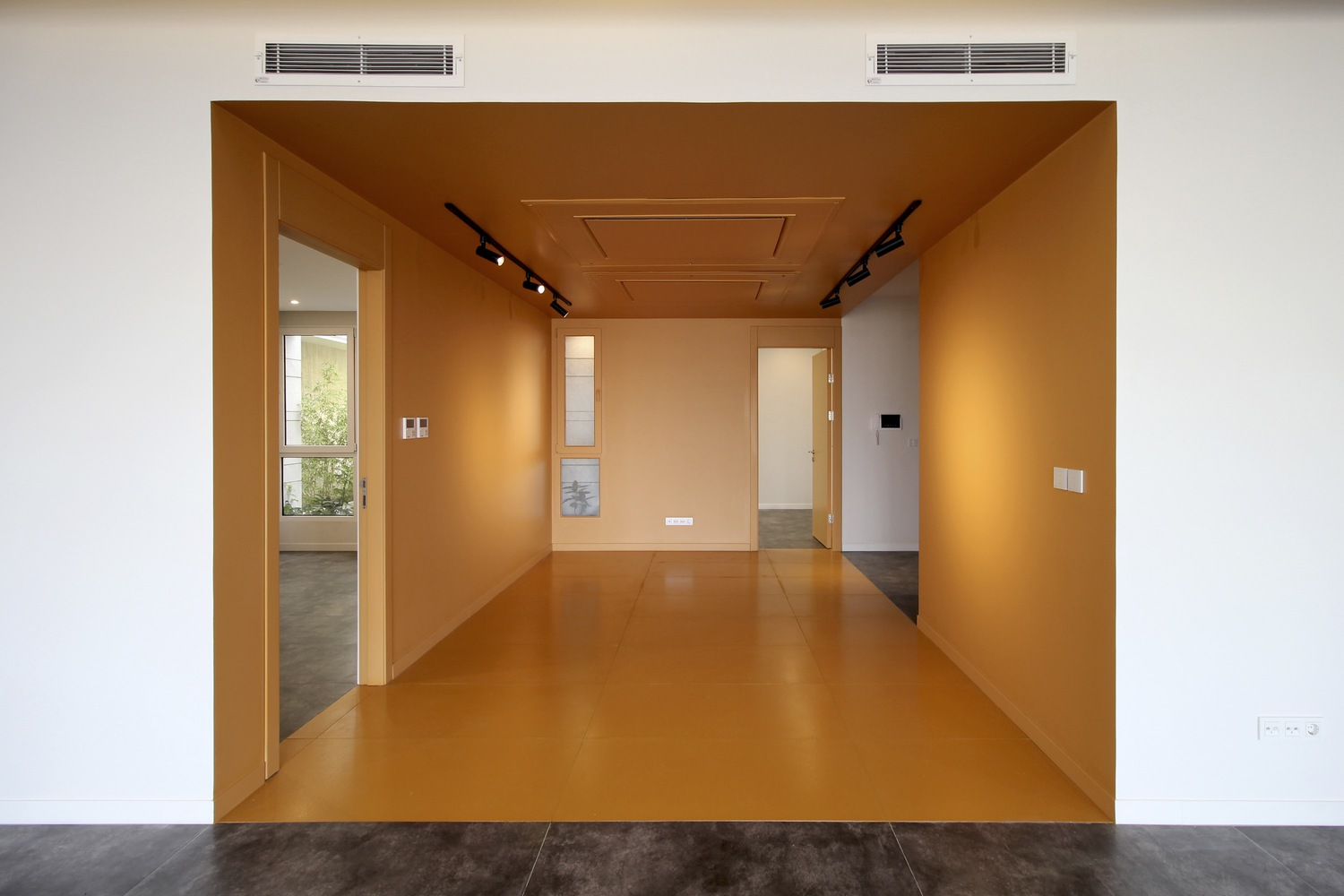 Orange volume: mustard-painted corridor and doors inserted into a white apartment, track lighting, minimal interior