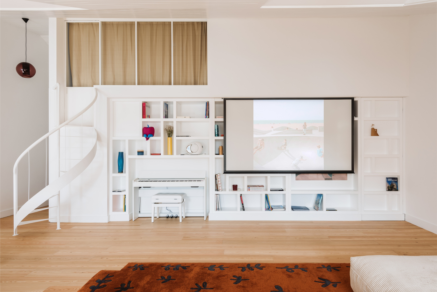 Built-in shelving wall with retractable screen and piano alcove beside spiral staircase
