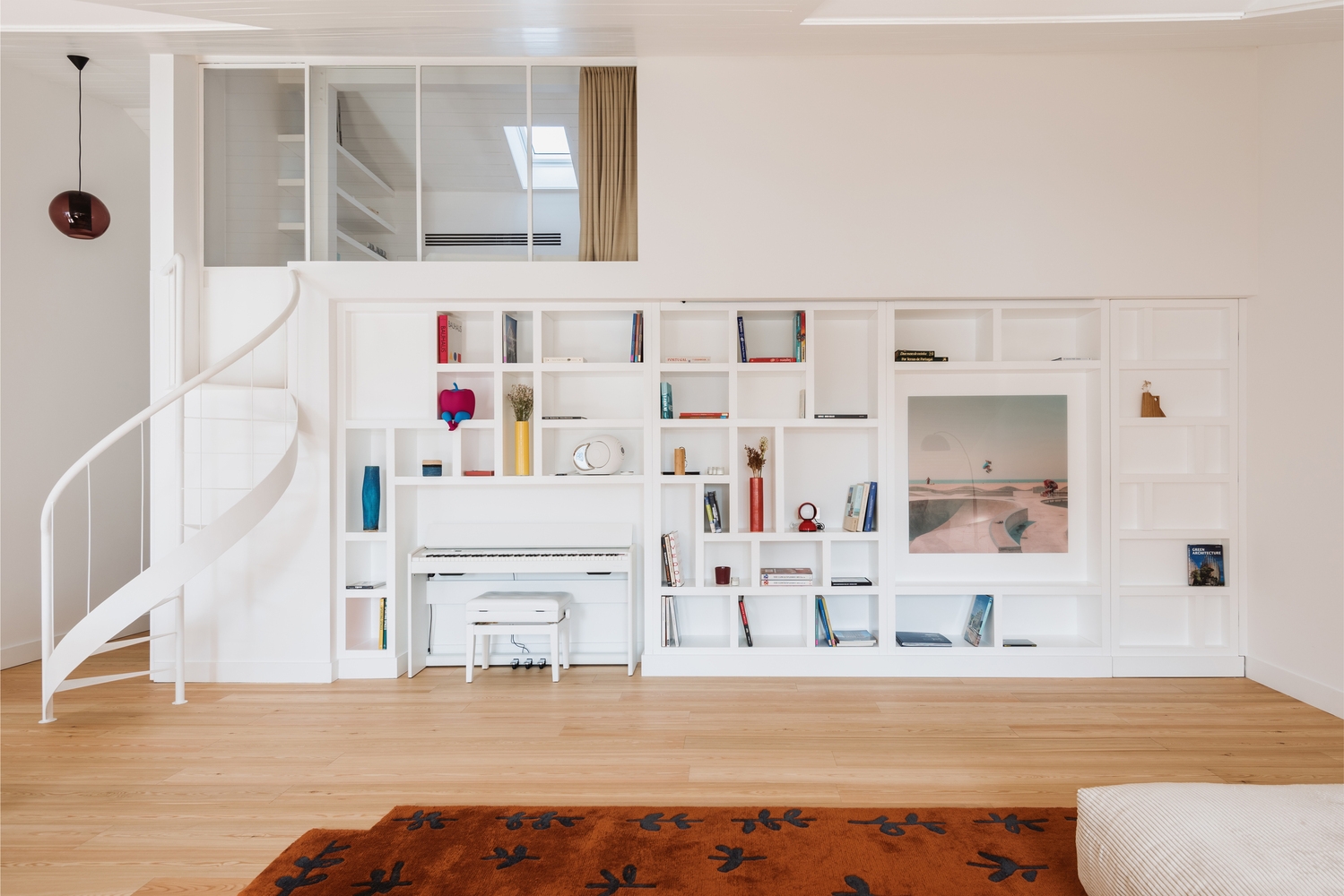 White built-in shelving wall with integrated piano niche and mezzanine window above spiral stair