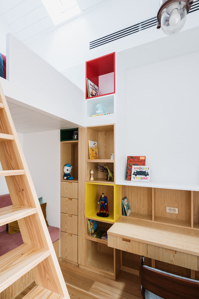Light wood storage wall with red and yellow cubbies beneath a double-height ceiling with skylight