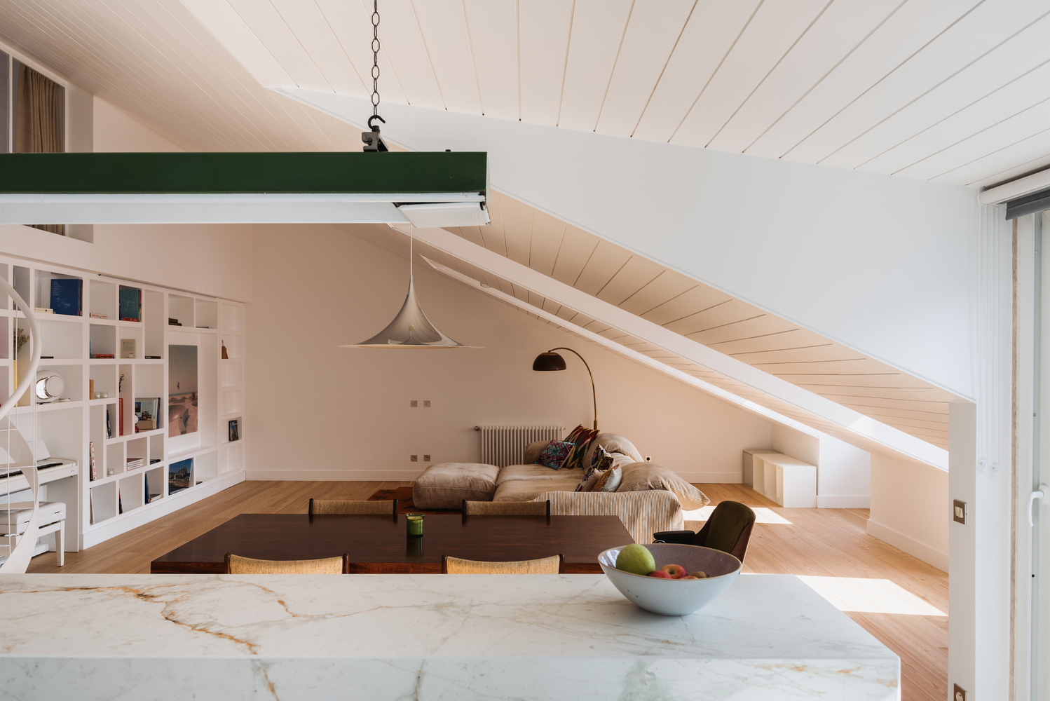 Open-plan living room beneath sloped ceiling with white marble island in foreground and pendant light