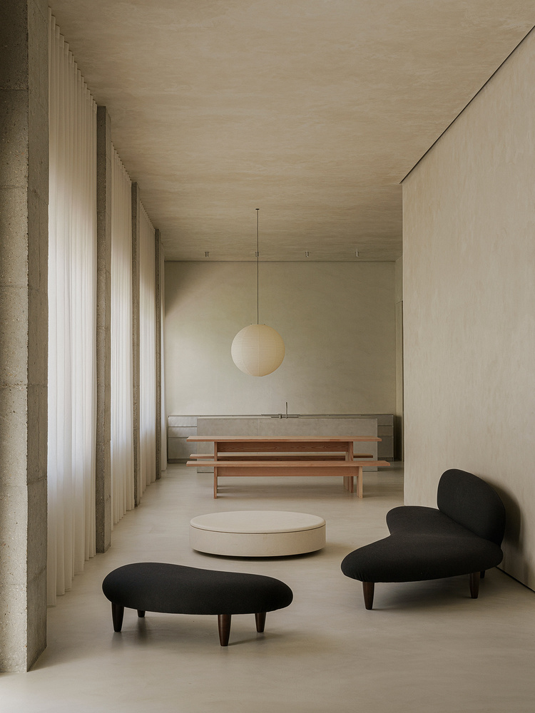Interior space with concrete columns, sheer curtains, timber benches and black upholstered seating under a sphere pendant