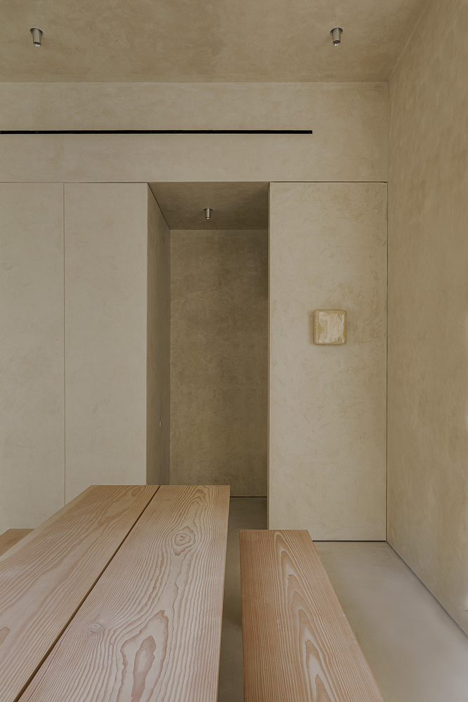 Timber dining bench extending toward a recessed alcove with flush wall panels and a small relief artwork