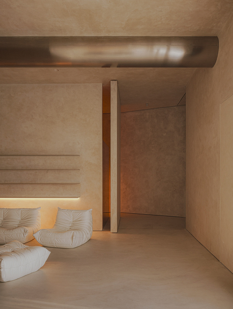 Living area with white upholstered sofa beneath an exposed cylindrical duct and textured plaster walls
