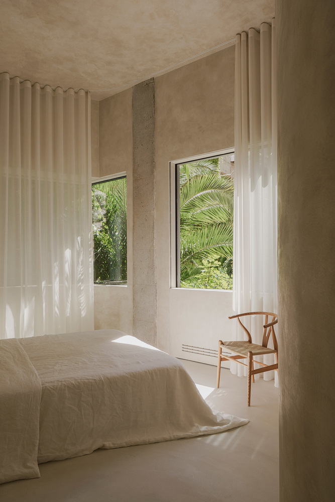 Bedroom with twin windows framing palm fronds and dappled sunlight on sheer curtains