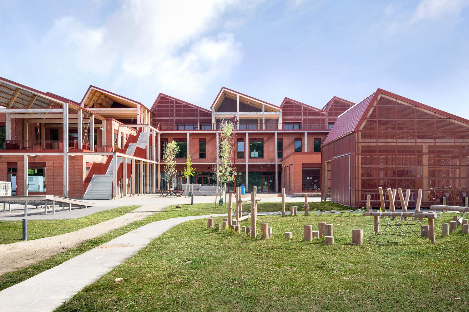 Aerial view: the full school complex on Gødvad Hill, red-brick pitched roofs stepping down the slope, forest behind