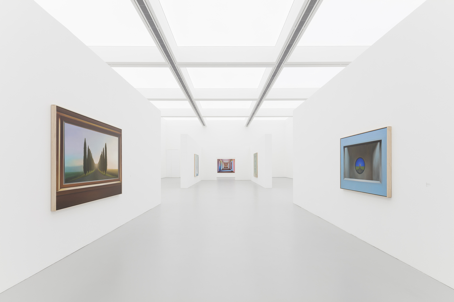 First-floor gallery: white walls, grey polished floor, linear skylight ceiling, paintings hung on freestanding partition walls
