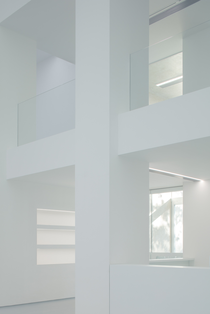 Atrium detail: white walls at multiple levels, glass balustrades, linear lights, window visible through layered openings